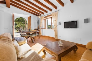 Una sala de estar con techo de madera, un televisor montado en la pared, una zona de comedor con una mesa y sillas, y un sofá.