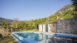 A swimming pool with stone walls, a small building with a green door, and a mountainous backdrop. - Holiday Home "Es Tarongers" with Mountain View, Garden, Terrace & Pool (Sóller)