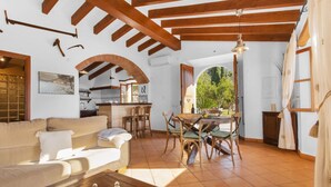 A spacious living area with a sofa, dining table, and chairs, wooden beams, and a view through an archway. - Holiday Home "Es Tarongers" with Mountain View, Garden, Terrace & Pool (Sóller)
