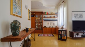 Una sala de estar con una mesa de centro de madera, un jarrón grande, estanterías, un televisor y una alfombra estampada.