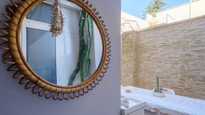 Una habitación con un espejo redondo, una ventana con cortina, una mesa con mantel y un cactus en maceta.