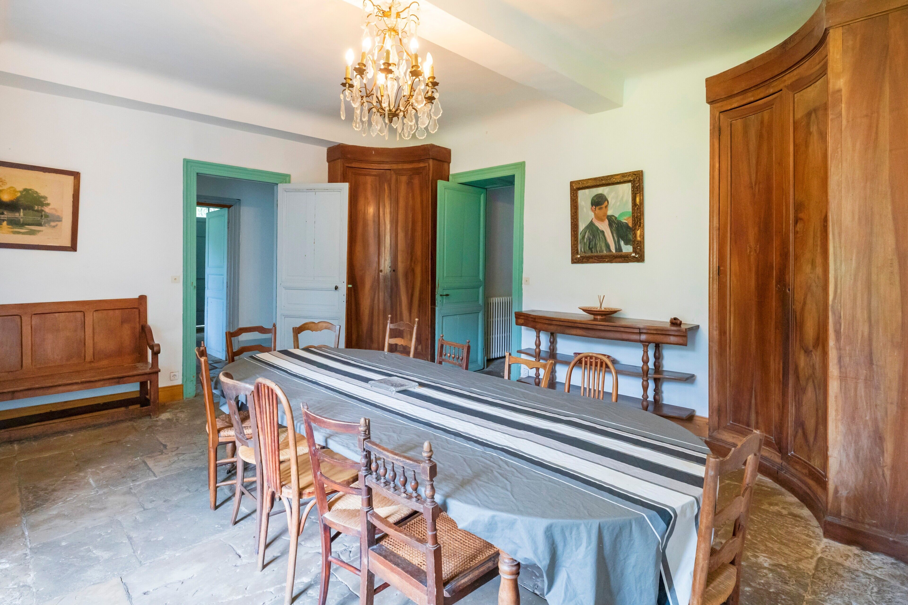 A dining room with a long table, wooden chairs, a chandelier, and a large wooden cabinet.