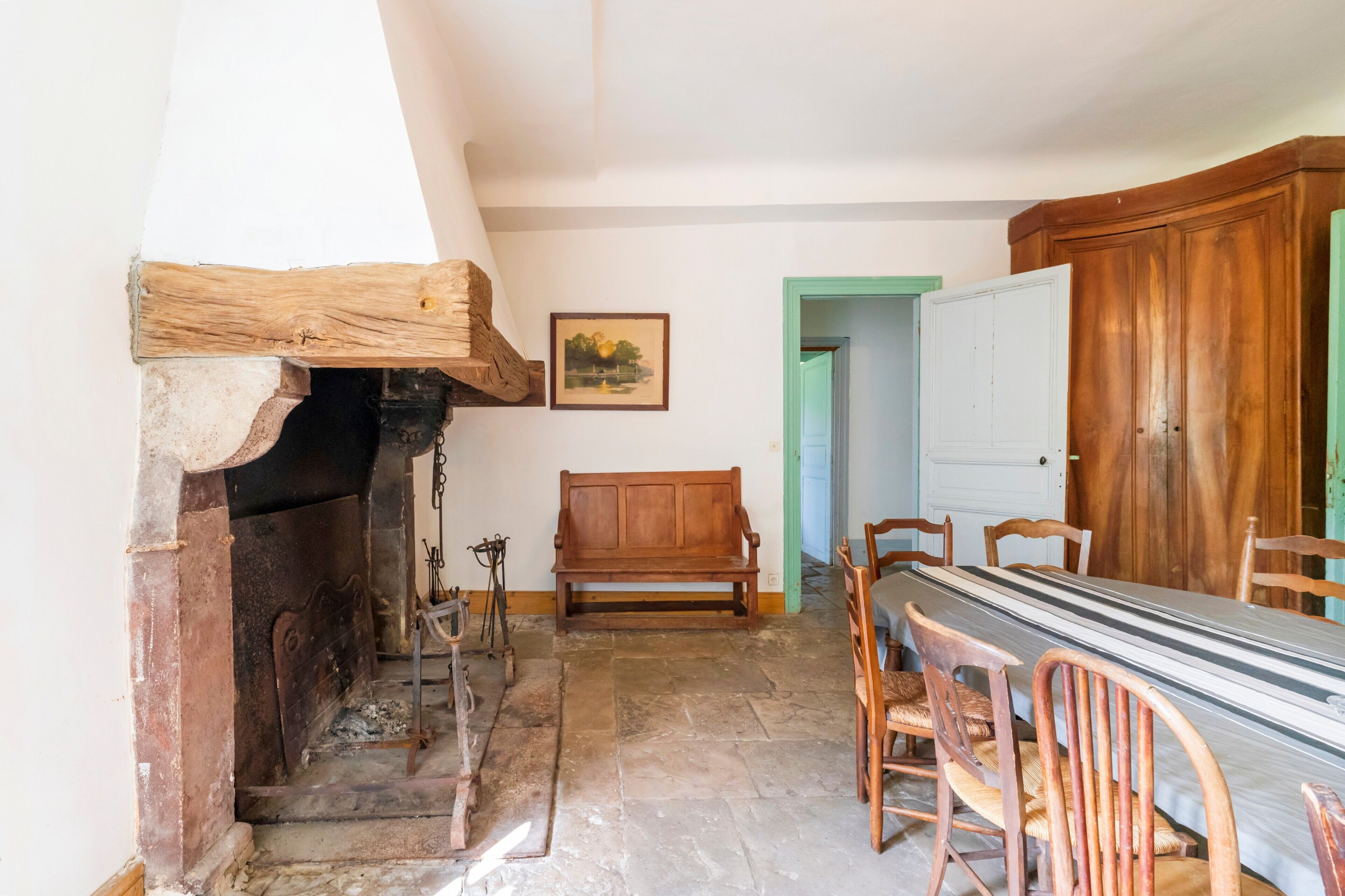 Een kamer met een open haard, een houten bank, een eettafel met stoelen en een houten garderobe.