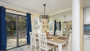 Een eetgedeelte met een grote tafel, witte stoelen en een kroonluchter. Er is een glazen schuifdeur naar een terras.