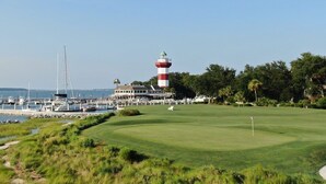 Een kustgolfbaan met een vuurtoren, een jachthaven en weelderige begroeiing.