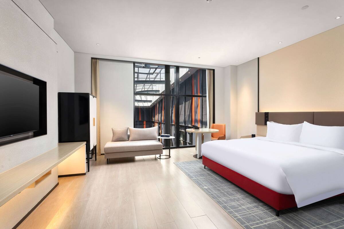 Una habitación de hotel moderna con una cama grande, un sofá, un televisor y una mesita.