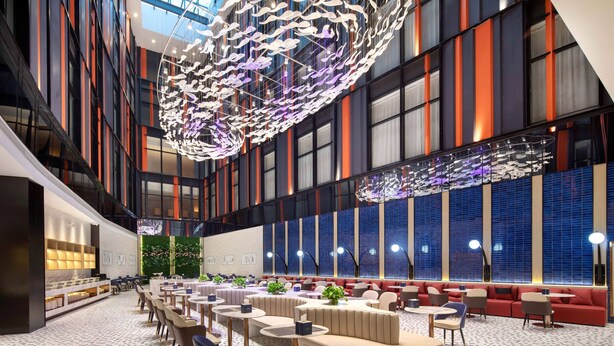 A spacious lobby with a modern design, featuring a large seating area with sofas and tables, a decorative ceiling installation, and large windows with blue-tinted glass. - Ramada By Wyndham Huzhou Wuxing (Huzhou)