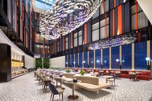 A spacious lobby with a modern design, featuring a large seating area with sofas and tables, a decorative ceiling installation, and large windows with blue-tinted glass. - Ramada By Wyndham Huzhou Wuxing (Huzhou)