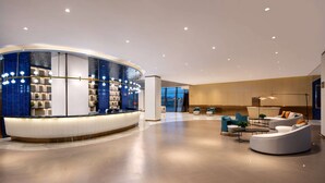 A modern lobby with a curved reception desk, seating area, and large windows. - Ramada By Wyndham Huzhou Wuxing (Huzhou)