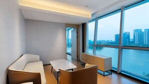 A modern hotel room with a large window, a sofa, a small table, and a cabinet. - Ramada By Wyndham Huzhou Wuxing (Huzhou)