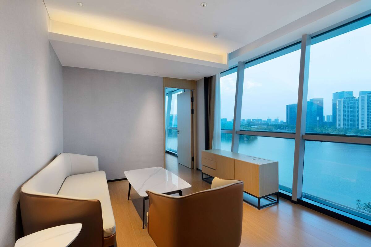 Una habitación de hotel moderna con un ventanal grande, un sofá, una mesita y un armario.
