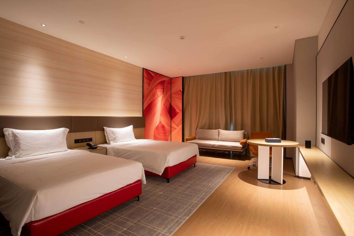 Habitación de hotel con dos camas, un sofá, una mesita y un televisor.