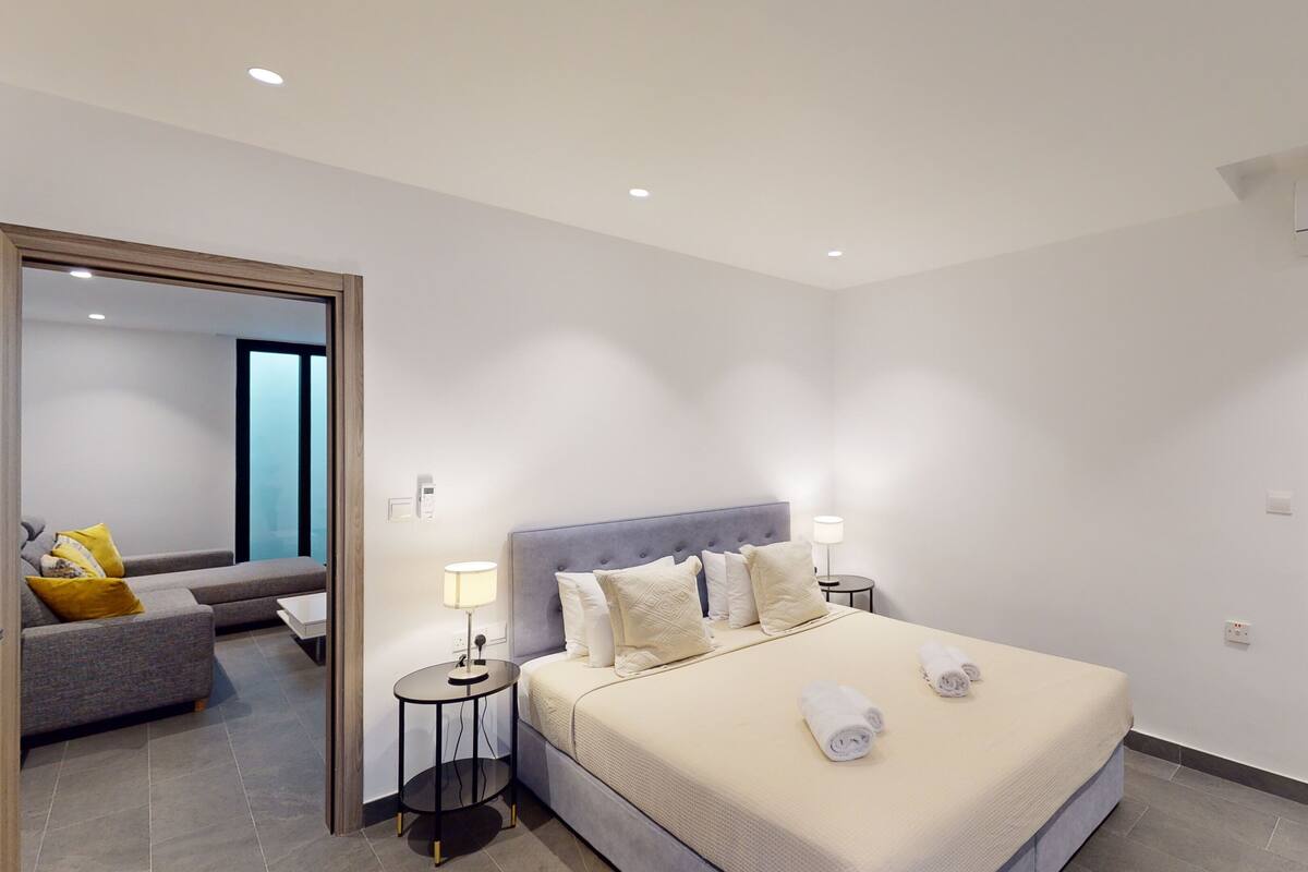 Une chambre d’hôtel moderne dotée d’un grand lit, de lampes de chevet, d’un canapé et d’une salle de bain avec des toilettes et une douche.