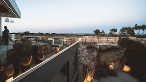 Un bâtiment moderne doté d’un balcon donnant sur un paysage rocheux et offrant une vue lointaine sur la mer.