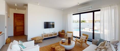 Una sala de estar moderna con televisor de pantalla plana, muebles de mimbre y vista a una piscina.