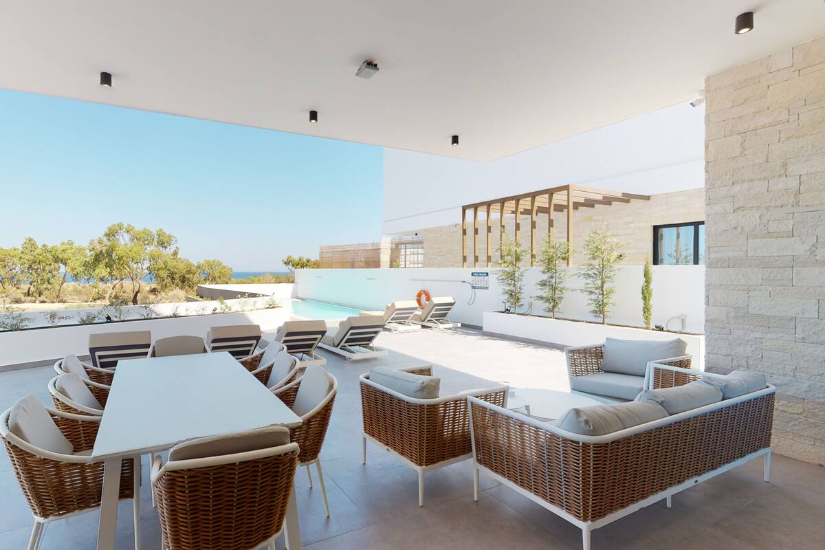 Une terrasse extérieure moderne, dotée d'une piscine, de meubles en osier et offrant une vue sur la mer.