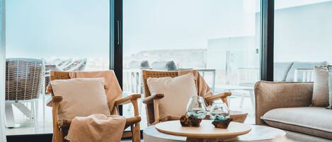 A modern living room with two wicker chairs, a round wooden table, and a sofa.