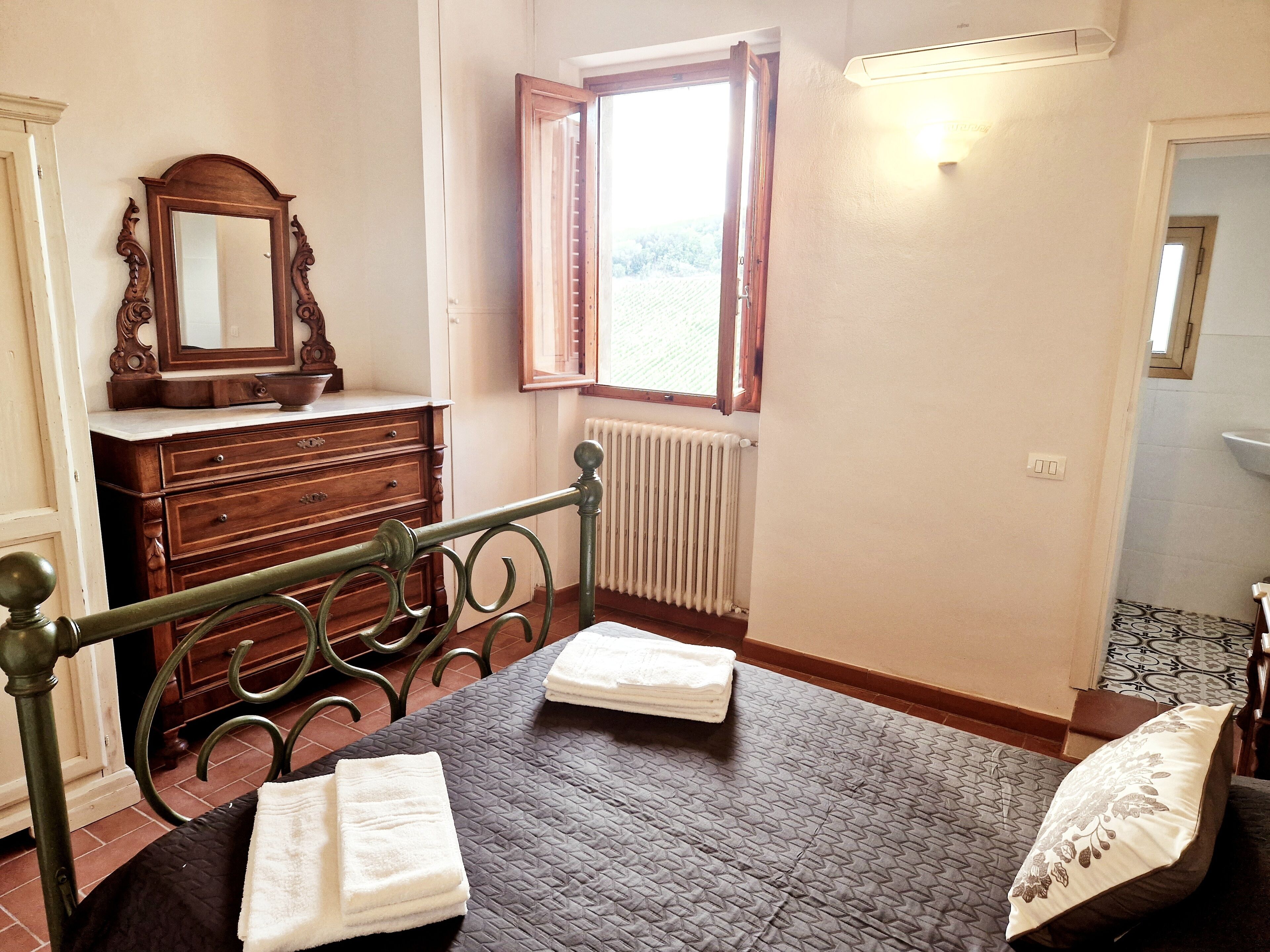 Ein Schlafzimmer mit Bett, Kommode, Spiegel, Fenster und Heizkörper.