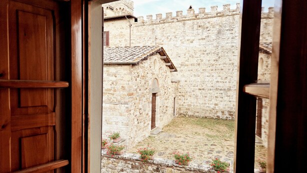 A view through a wooden door of a courtyard with stone walls and potted plants.