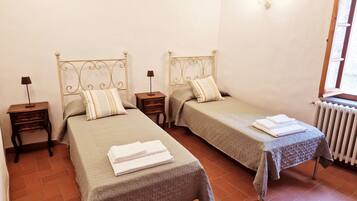 A room with two beds, each with a nightstand and a lamp. There is a window with a view of the outside.
