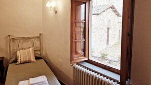 A bedroom with a bed, a radiator, a window, and a wall-mounted light fixture.