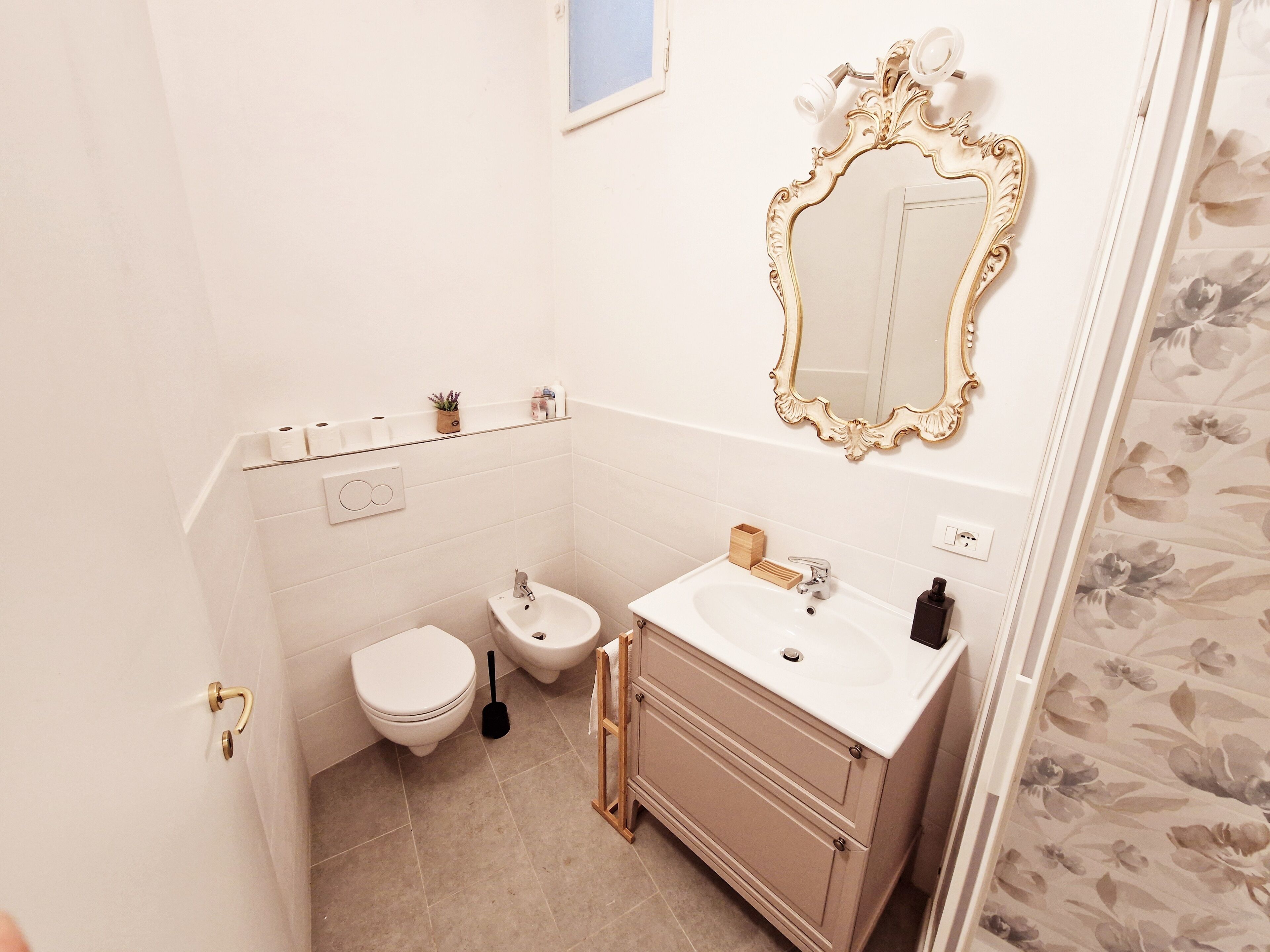 Une petite salle de bain comprenant des toilettes, un bidet, un meuble-lavabo avec un miroir et une petite étagère avec des articles de toilette.