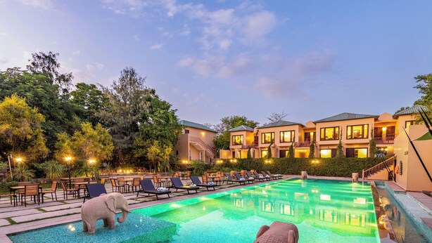 Zona de piscina de hotel con sillones de descanso y una estatua decorativa de elefante.
