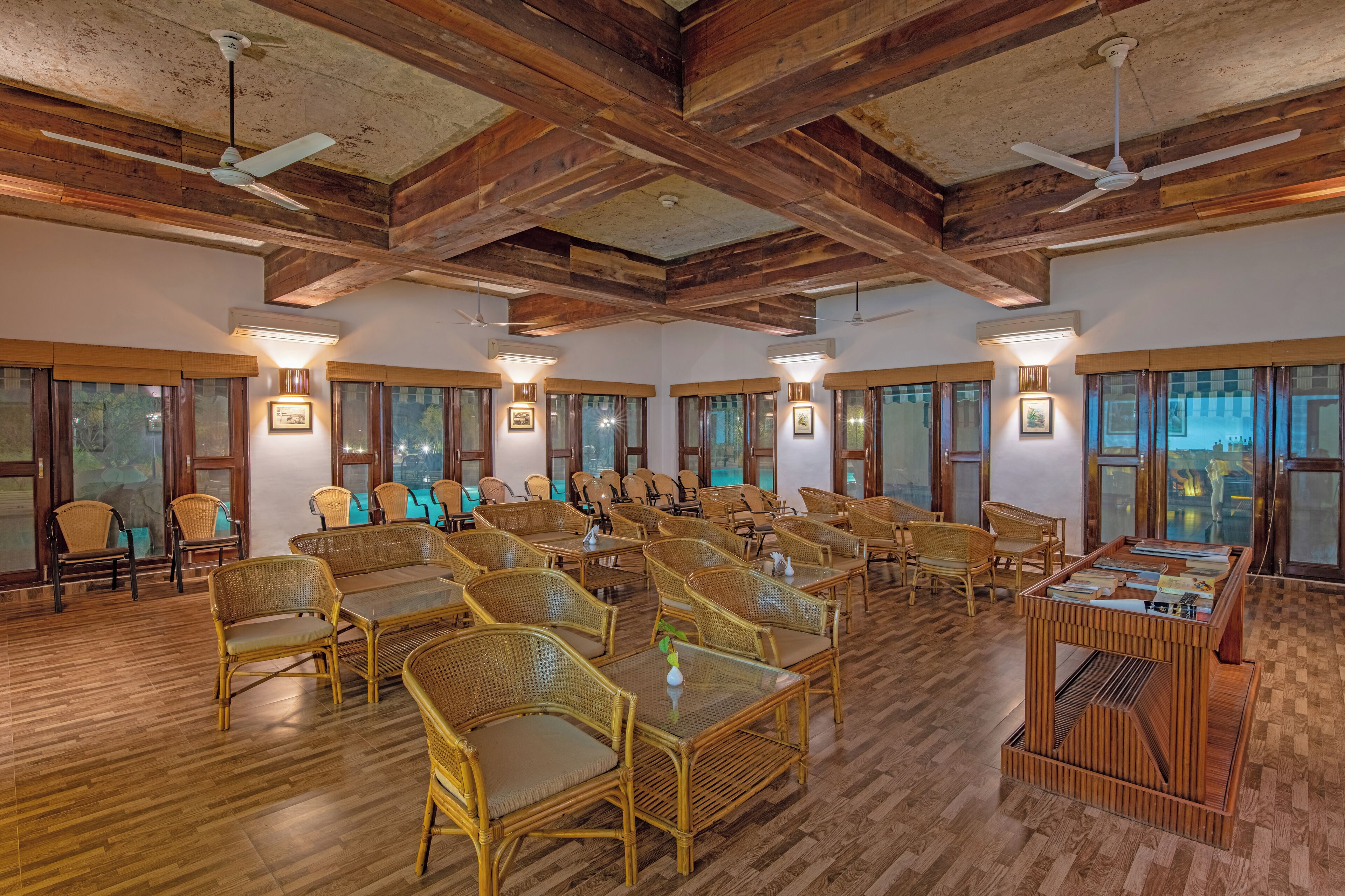 A spacious room with wooden floors, multiple seating arrangements, ceiling fans, and large windows.