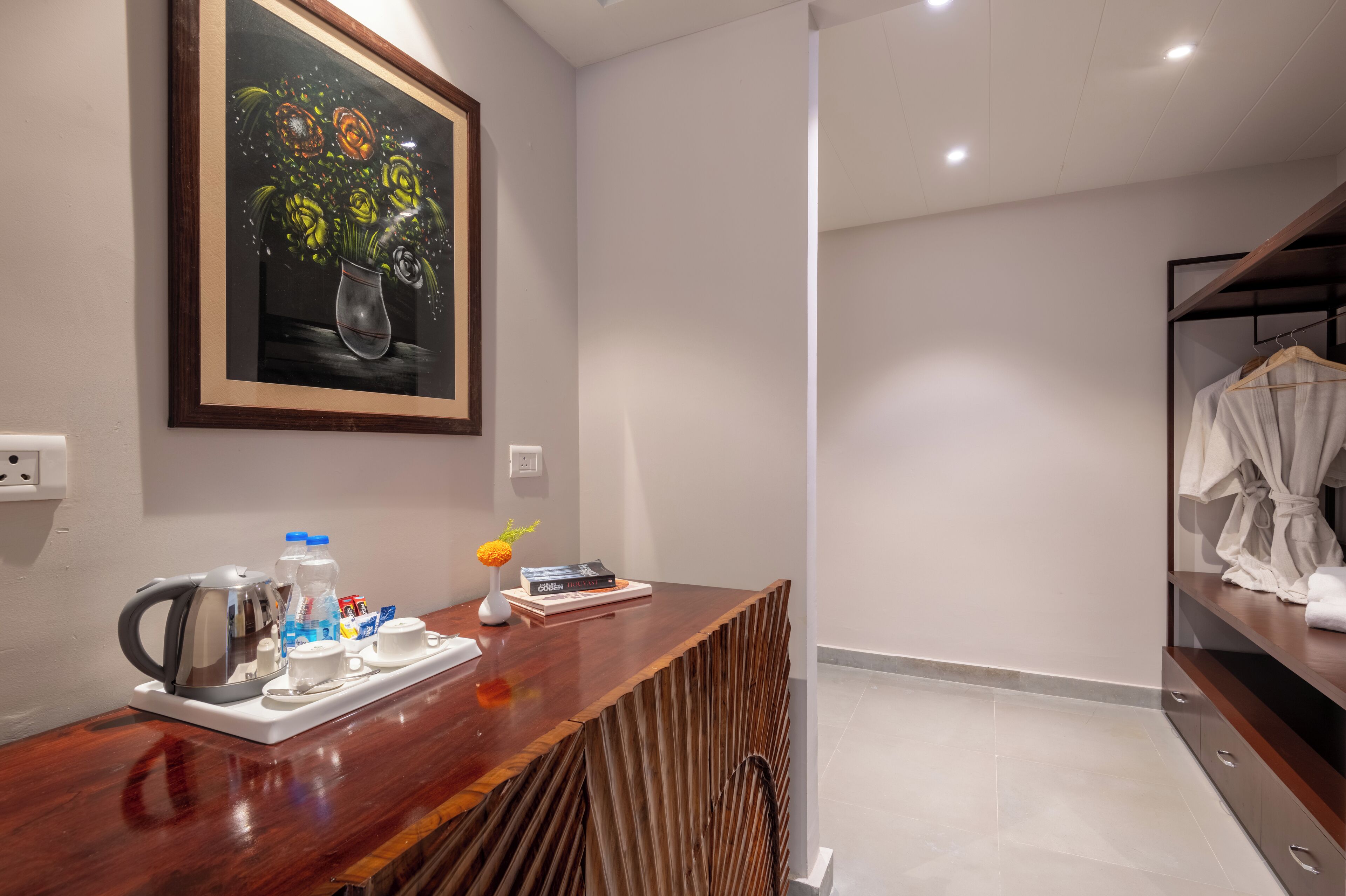 Zona de recepción de un hotel moderno con un mostrador de madera, un cuadro enmarcado con flores, una tetera, botellas de agua y un libro.
