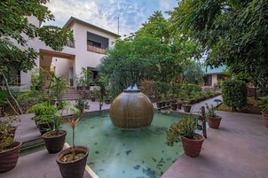 Un patio central con una fuente, rodeado de plantas en macetas y un edificio con balcones.