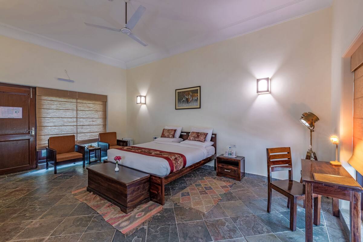 Une chambre d’hôtel équipée d’un lit, d’un bureau, d’une chaise, d’une table de chevet, d’une lampe et d’un ventilateur de plafond.