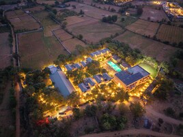 Vista aérea de una extensa propiedad bien iluminada, con varios edificios, piscina y campos circundantes.