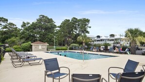 A pool area with lounge chairs, a small gazebo, and a building in the background.