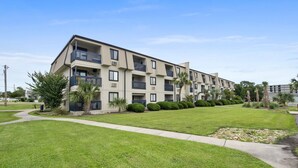 A multi-story apartment building with balconies, a well-maintained lawn, and a clear sky.