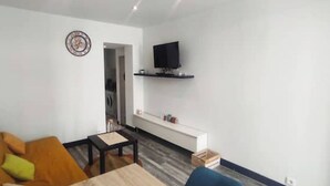 Un saló amb un sofà, una taula de centre, una televisió sobre un suport i una paret blanca amb un rellotge.