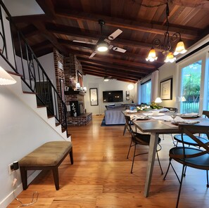 Un interior moderno con una escalera de madera, una zona de comedor con una mesa y sillas, y una sala de estar con un sofá y televisor.
