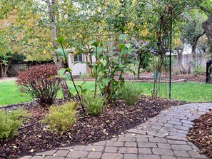 Un camino pavimentado en un jardín con varias plantas y una valla de madera al fondo.