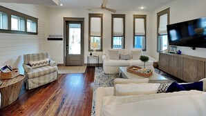 Ein geräumiges Wohnzimmer mit Deckenventilator, Flachbildfernseher und großem Fenster mit Jalousien.