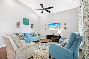 A living room with a sofa, armchairs, a coffee table, and a ceiling fan.