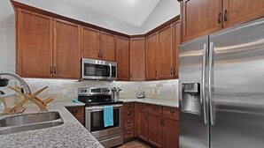 Una cocina con gabinetes de madera, electrodomésticos de acero inoxidable, encimeras de granito y un horno empotrado.