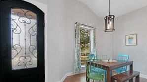 Un comedor con una mesa de madera, sillas verdes y azules, un banco, una lámpara colgante y una puerta con detalles de vidrio.