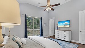 Un dormitorio con cama, ventilador de techo, televisor y ventana con cortinas.