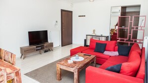 A living room with a red sofa, wooden coffee table, and a TV on a wooden stand. - Delightful Apartment with amazing view (Elliniko-Argyroupoli)