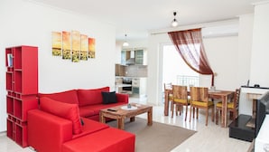 A modern living room with a red sectional sofa, a wooden coffee table, and a dining area with wooden chairs and a table. - Delightful Apartment with amazing view (Elliniko-Argyroupoli)
