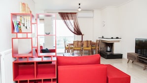A modern living room with a red sectional sofa, a wooden dining table with chairs, a TV, and a fireplace. - Delightful Apartment with amazing view (Elliniko-Argyroupoli)