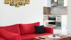 A modern living room with a red sofa, a wooden coffee table, and a kitchen in the background. - Delightful Apartment with amazing view (Elliniko-Argyroupoli)
