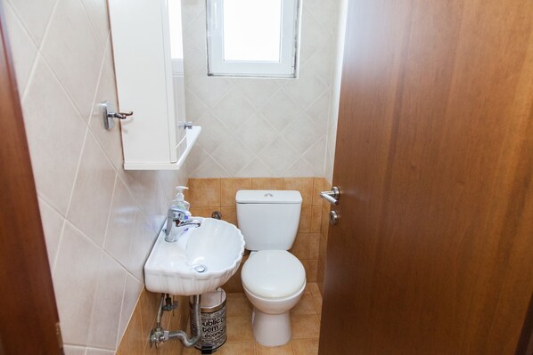 A small bathroom with a white sink, toilet, and a window above the toilet.