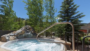 Un bain à remous agrémenté d’une cascade en pierre, entouré d’arbres et surplombant un ciel dégagé.