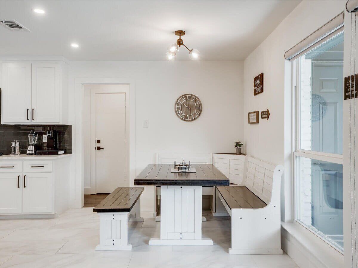 A modern kitchen with white cabinetry, a central island, and a dining area with benches.