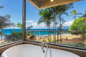 Een badkamer met een bad en uitzicht op het strand en de oceaan door een groot raam.